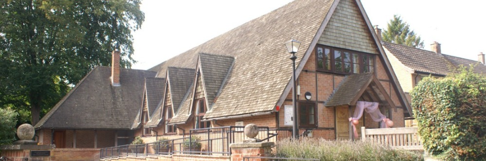 The hall's long shingled roofline and gabled windows, decorated with pink bows for a wedding