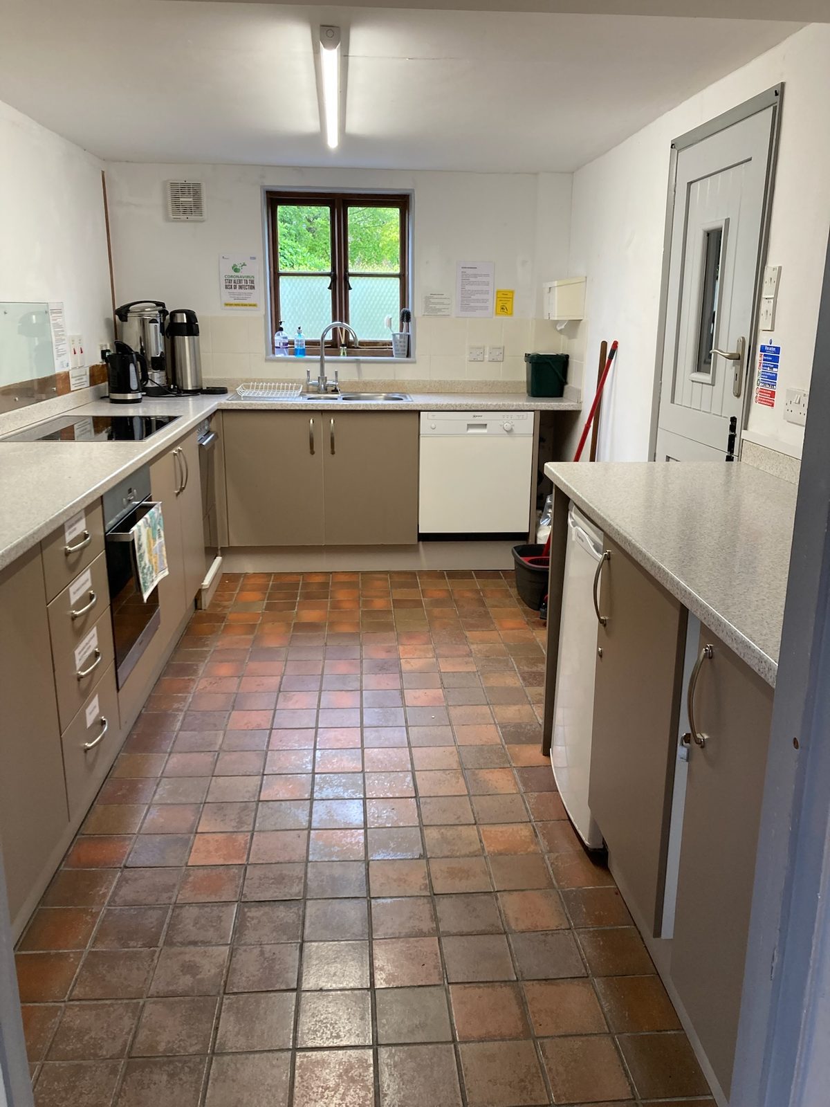 The kitchen: beige units around a quarry-tiled floor, with a double sink beneath the window, oven, hob, dishwasher, fridge and hot-water urn