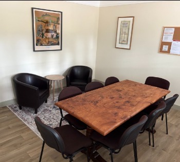 The Library Room: a polished wooden meeting table with eight chairs, two leather armchairs, and framed prints