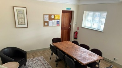 The Library Room from the armchair corner: meeting table, window with blinds, and noticeboard