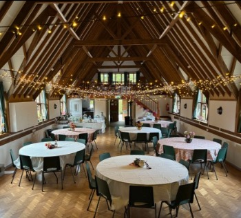 Round tables with pink cloths beneath swags of fairy lights, looking towards the gallery staircase