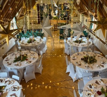 Round tables in white linen with greenery centrepieces, gold and silver stars hanging from the beams