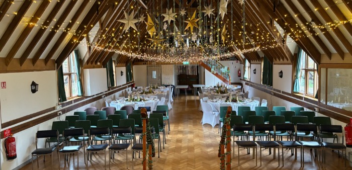 The hall arranged for a ceremony: rows of chairs at the front, dressed dining tables behind, stars and fairy lights above