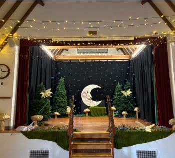 The raised stage dressed as a theatre set with a smiling crescent moon, trees and a starry backdrop