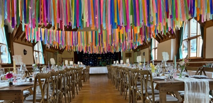 The full hall set for a wedding breakfast, hundreds of bright ribbons hanging above long tables
