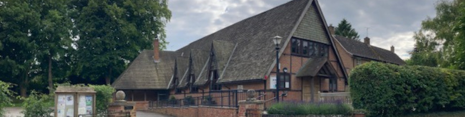 The village hall seen from the road, with its steep tiled roof and the village noticeboard in front