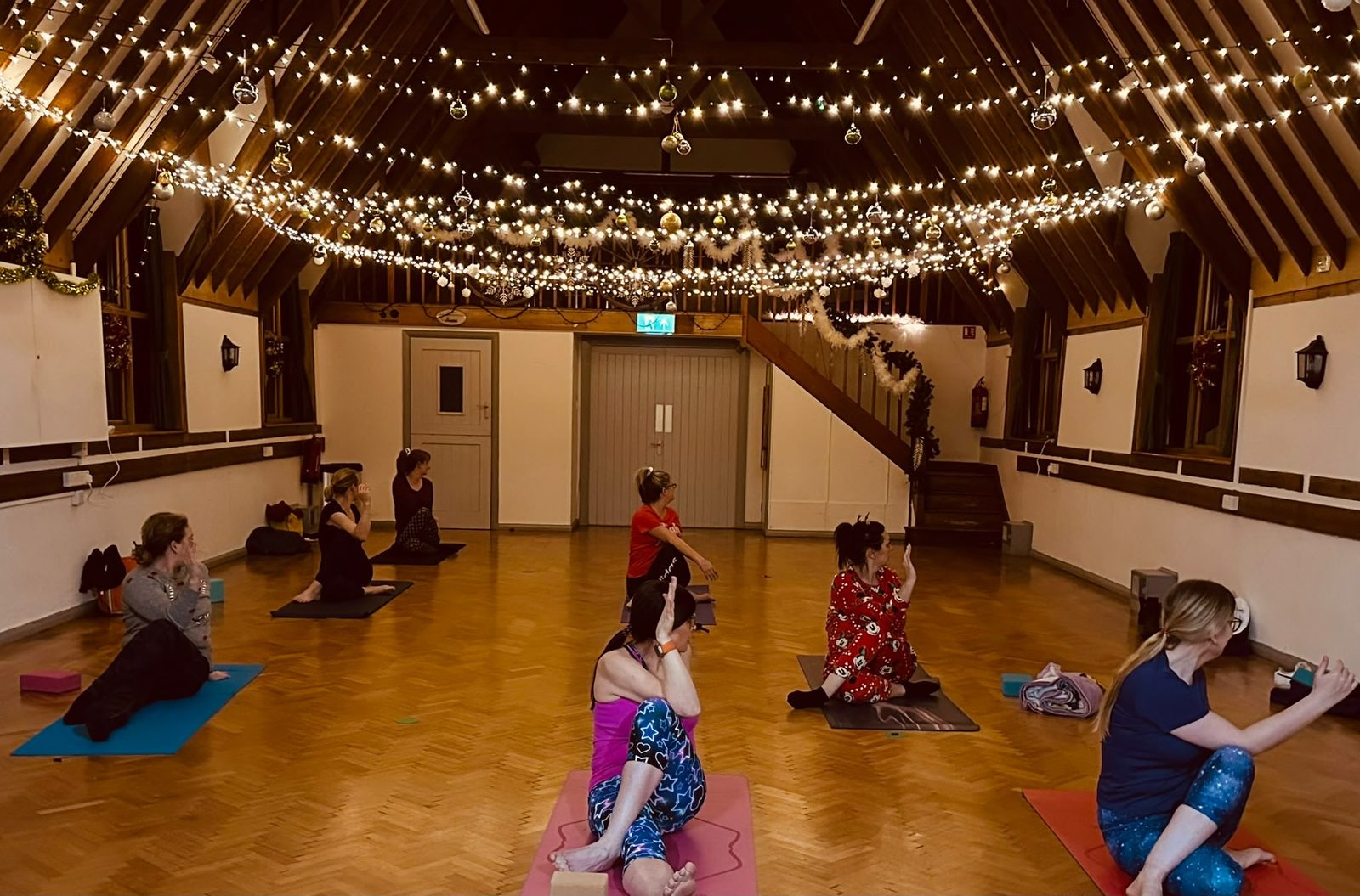 A yoga class mid-pose on mats under fairy lights and festive decorations in the main hall