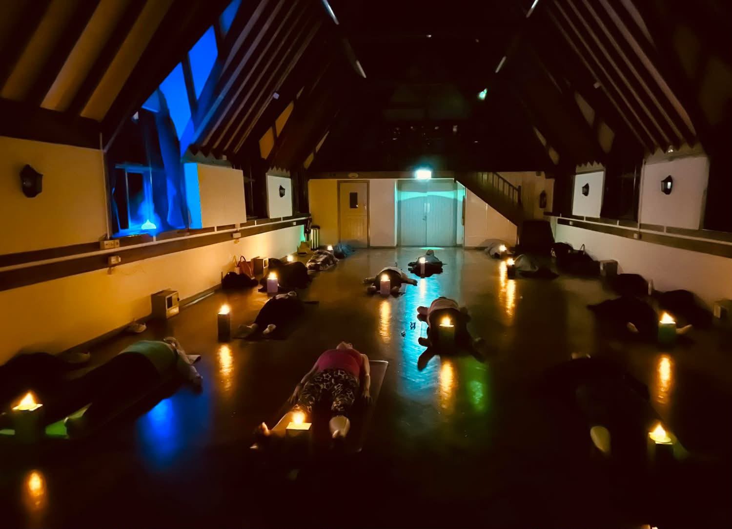 A candlelit relaxation: people lying on mats in the darkened hall with candles glowing beside each mat